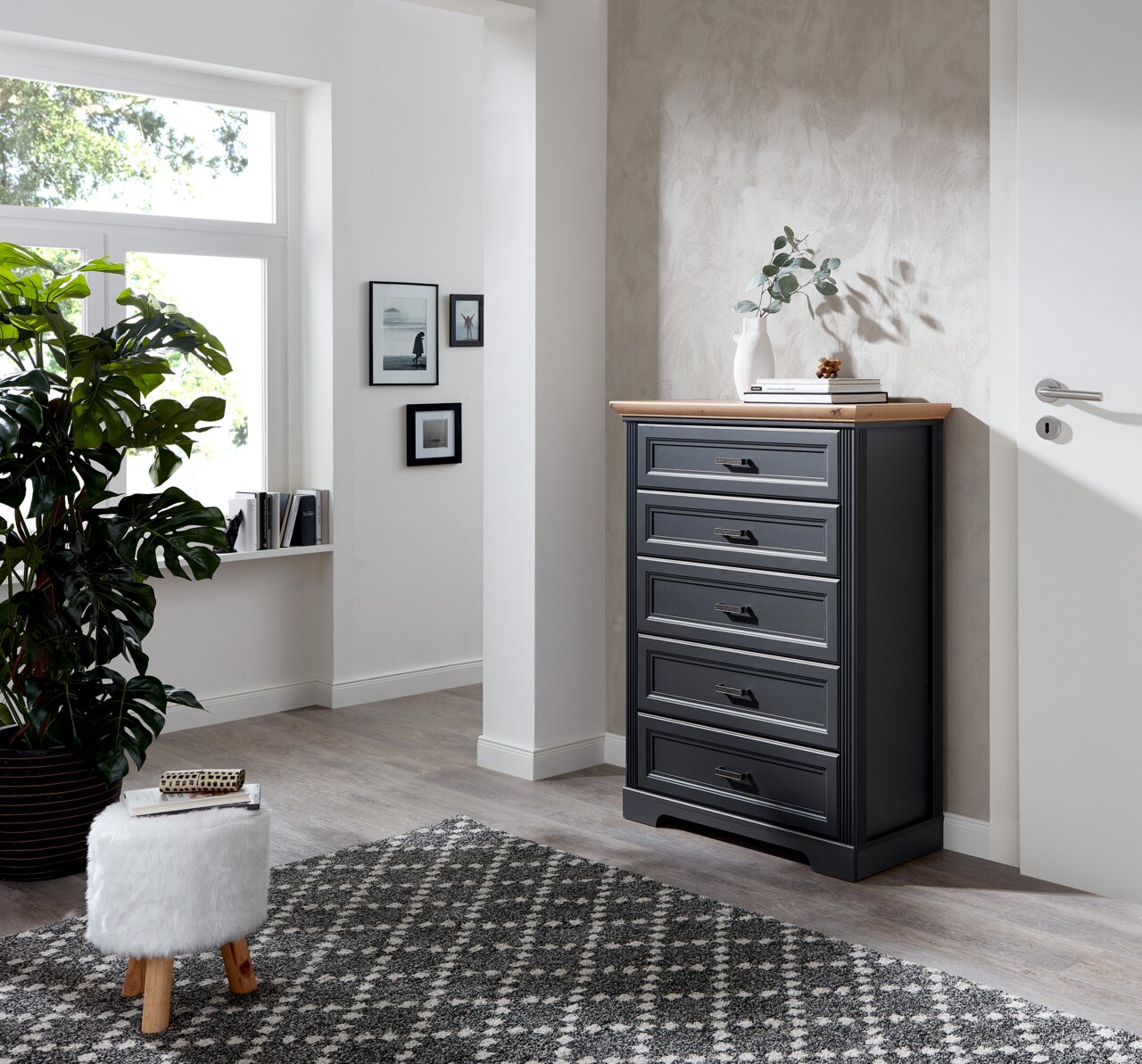 Schubkastenkommode in einem modernen Wohnzimmer, seitliche Perspektive, mit fünf Schubladen und einer Holzplatte, dekoriert mit einer Vase und Büchern.