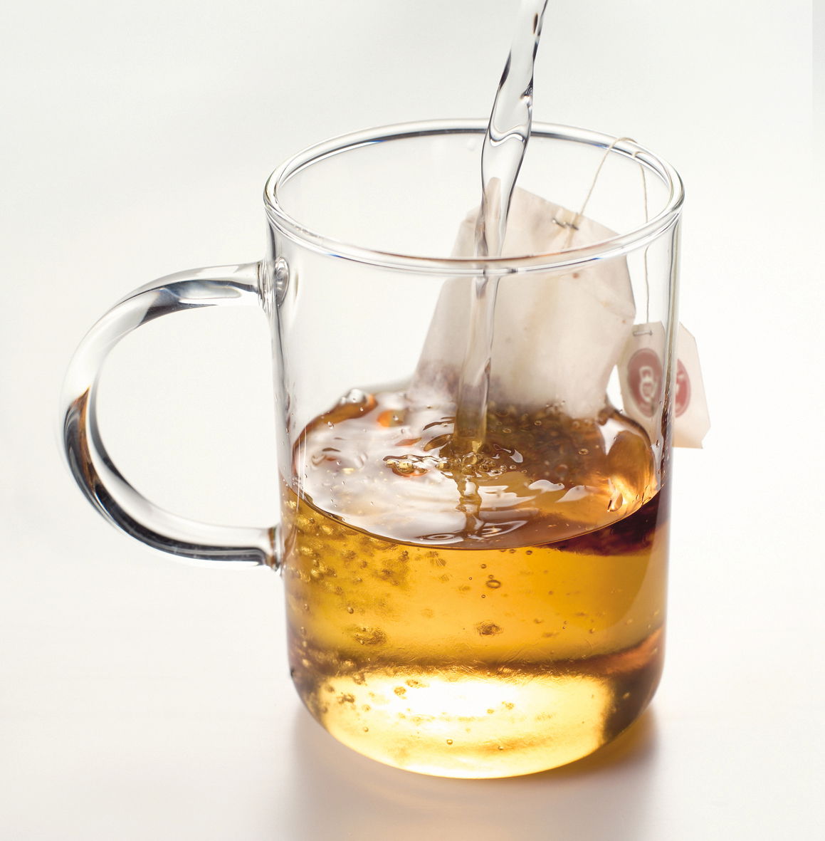 Teeglas Novo 360ml mit Henkel, von der Seite fotografiert, während heißes Wasser über einen Teebeutel gegossen wird.