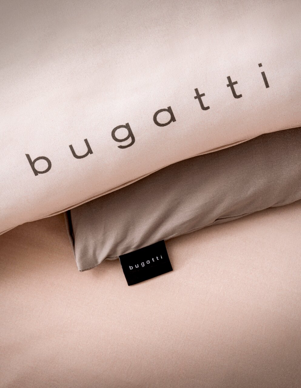 Close-up van beige beddengoed met het opschrift 'bugatti' op een kussensloop.