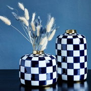 Zwei handbemalte Vasen im Harlekin-Muster mit goldenen Rändern, eine mit Trockenblumen, auf einem Tisch vor blauem Hintergrund, seitliche Perspektive.