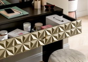 Nahaufnahme eines Schminktisches mit geöffneter Schublade, die verschiedene Kosmetikartikel und Accessoires enthält. Die Schubladenfront hat ein geometrisches Muster. Perspektive von schräg oben.