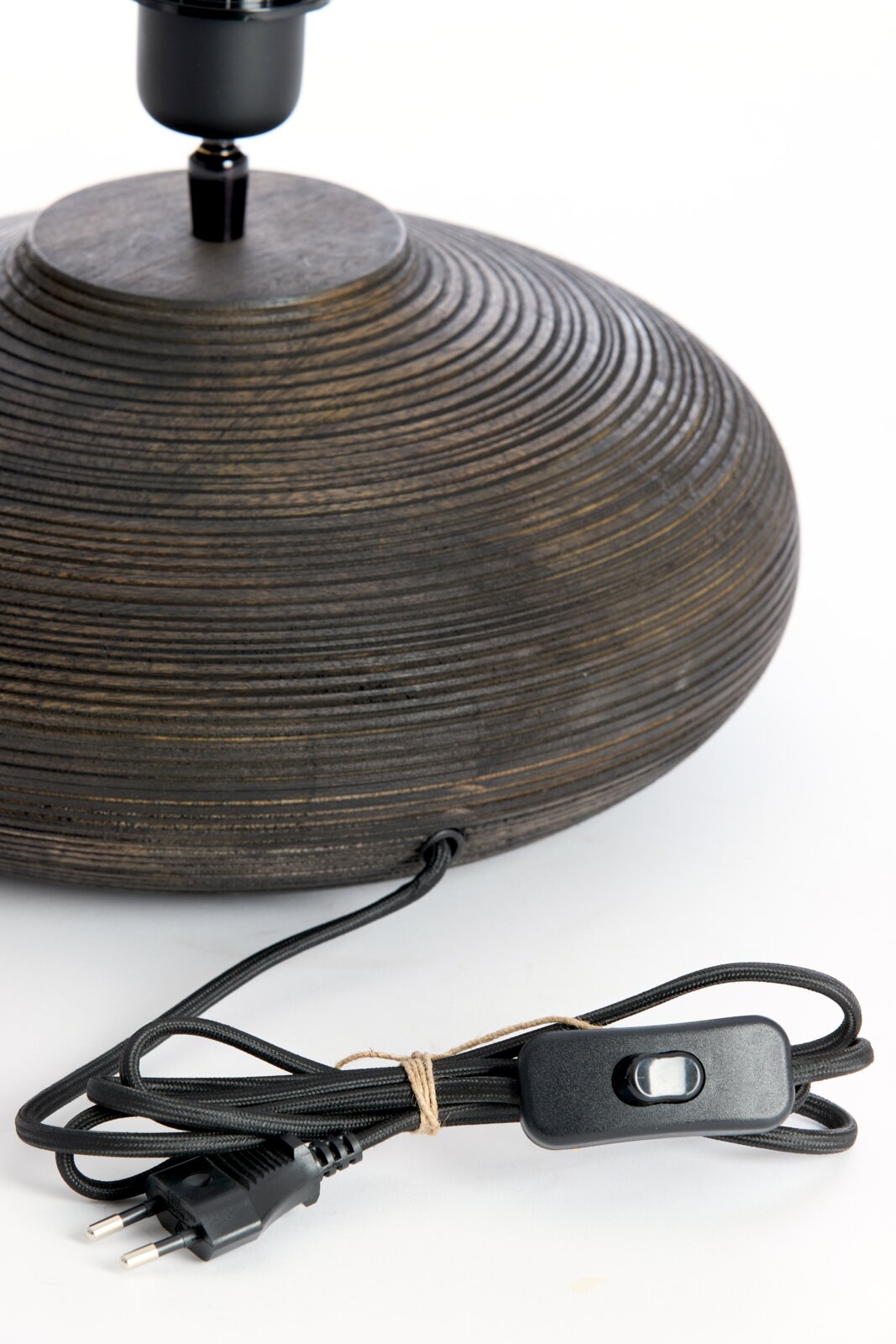 Close-up van een ronde, geribbelde lampvoet van donker hout met een zwarte kabel en schakelaar op de voorgrond.