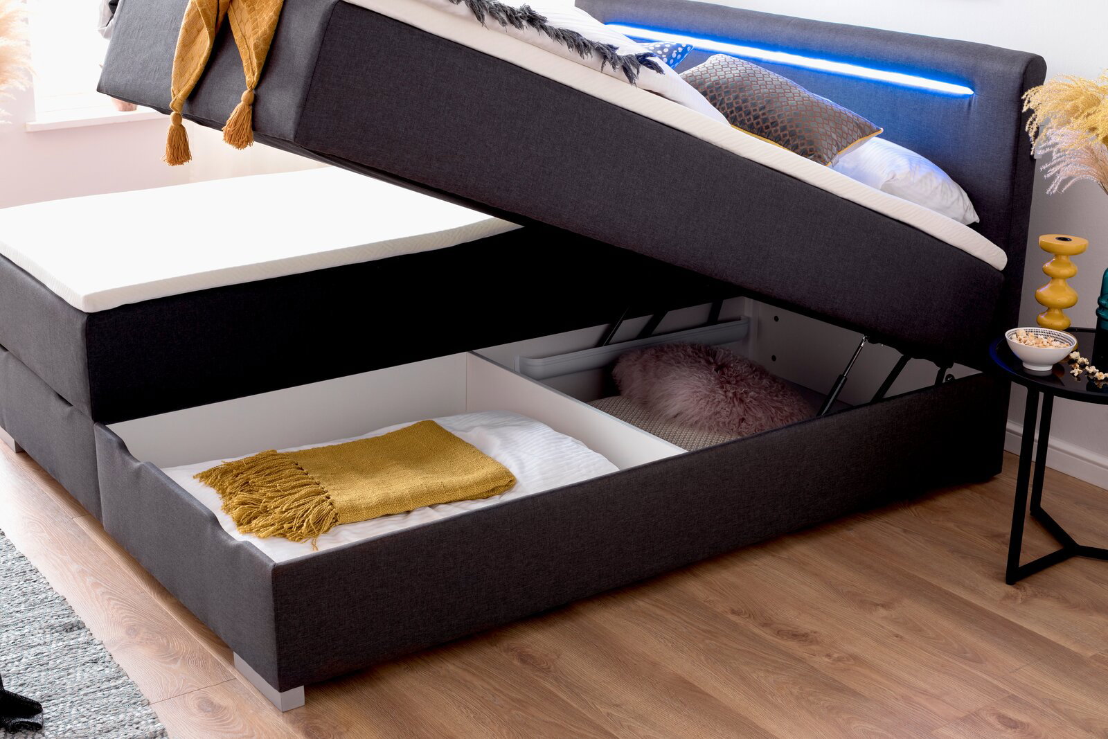 Boxbett mit hochgeklappter Matratze, darunter Stauraum mit Decken und Kissen, seitliche Perspektive