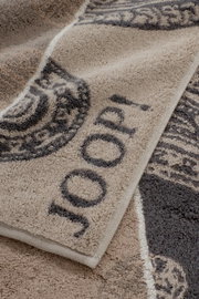 Nahaufnahme eines weichen Frottee-Handtuchs in Beige und Grau mit gewebtem Muster und Schriftzug, perspektivisch schräg von oben fotografiert