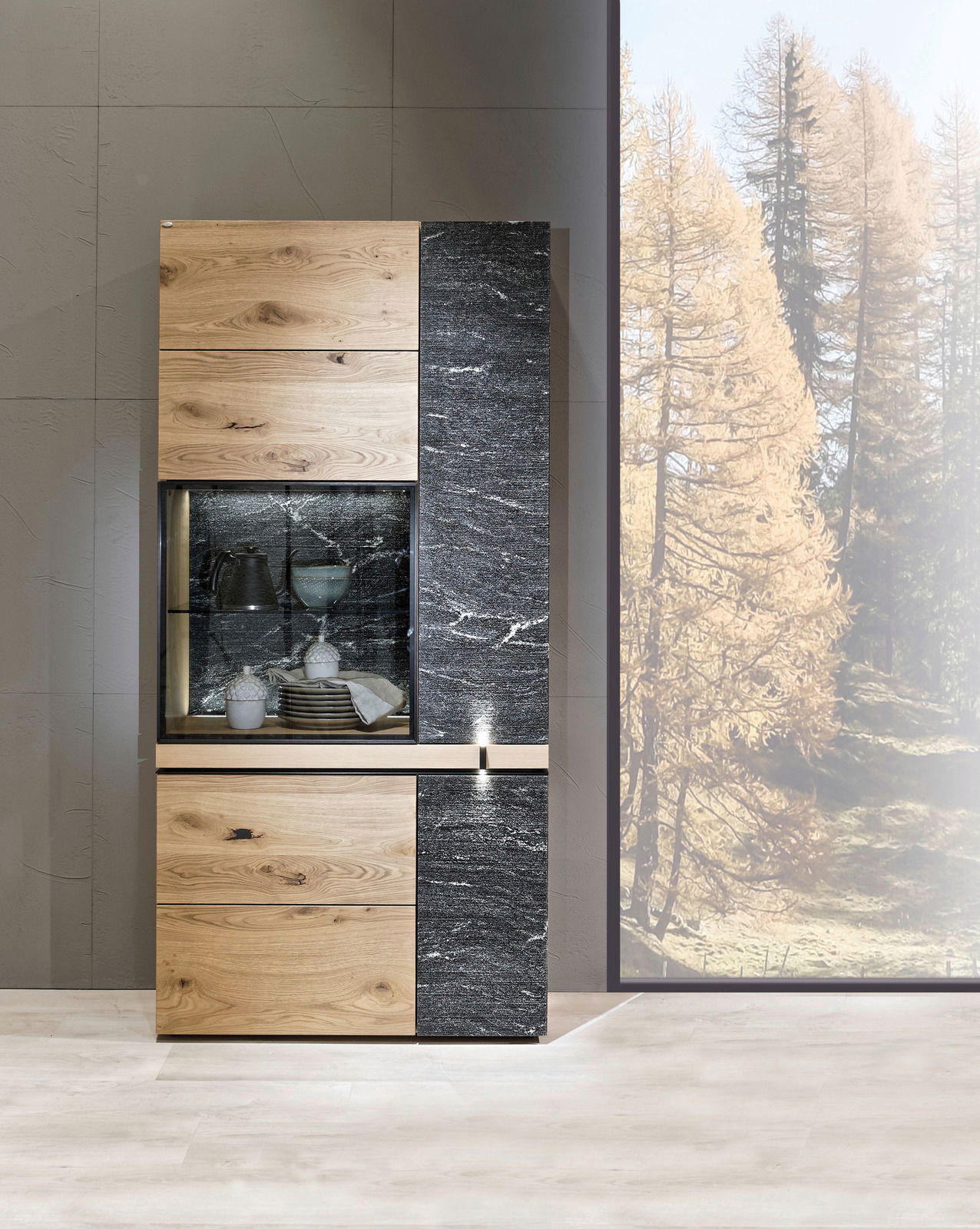 Moderne Vitrine aus Holz und Stein mit Glasfront, frontal fotografiert, im Hintergrund ein Fenster mit Blick auf Bäume.