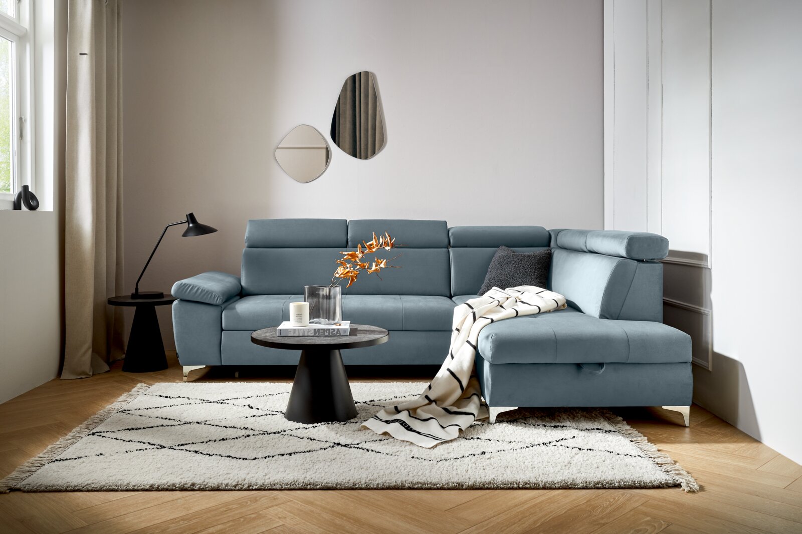Moderne L-vormige hoekbank in een stijlvolle woonkamer, met blauwe bekleding, versierd met kussens en een deken, gezien vanuit het perspectief linksvoor.