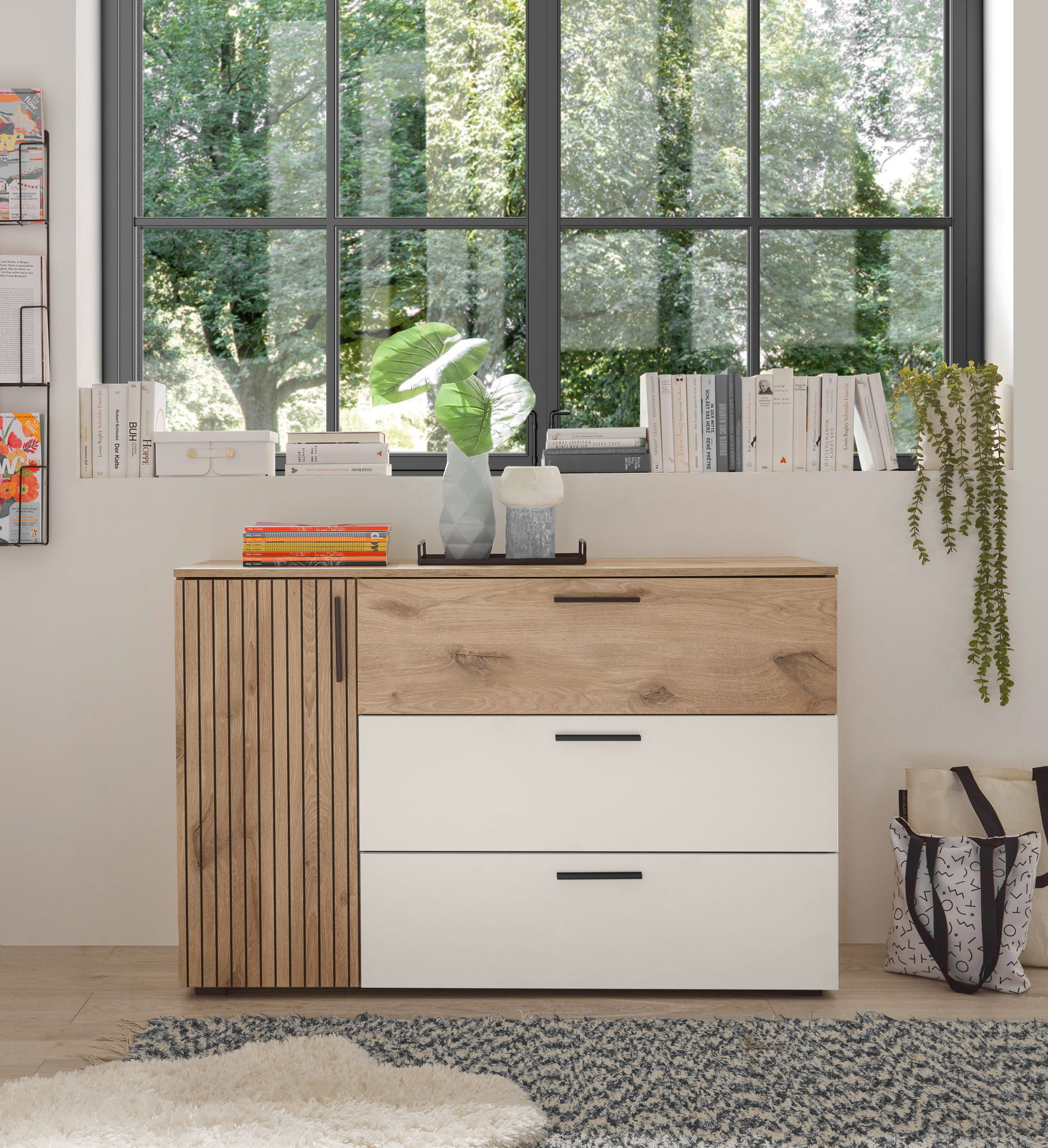 Kommode mit Holz- und Weißtönen, frontal fotografiert, vor einem Fenster mit Blick ins Grüne.