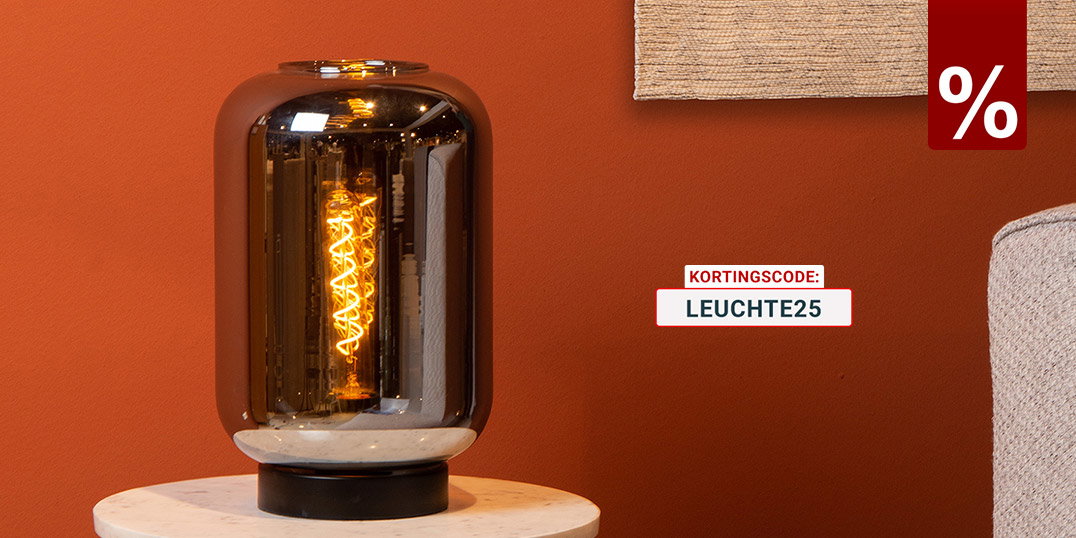 Moderne tafellamp met rookglas en een warm vintage lichtbron op een ronde bijzettafel voor een terracottakleurige muur.