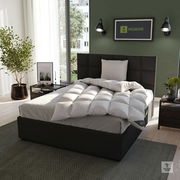 Gemütliches Schlafzimmer mit einem modernen Bett, das mit einer weißen, gesteppten Cassettendecke und einem passenden Kissen ausgestattet ist. Die Perspektive zeigt das Bett von schräg vorne, umgeben von stilvoller Dekoration und einem großen Fenster im H