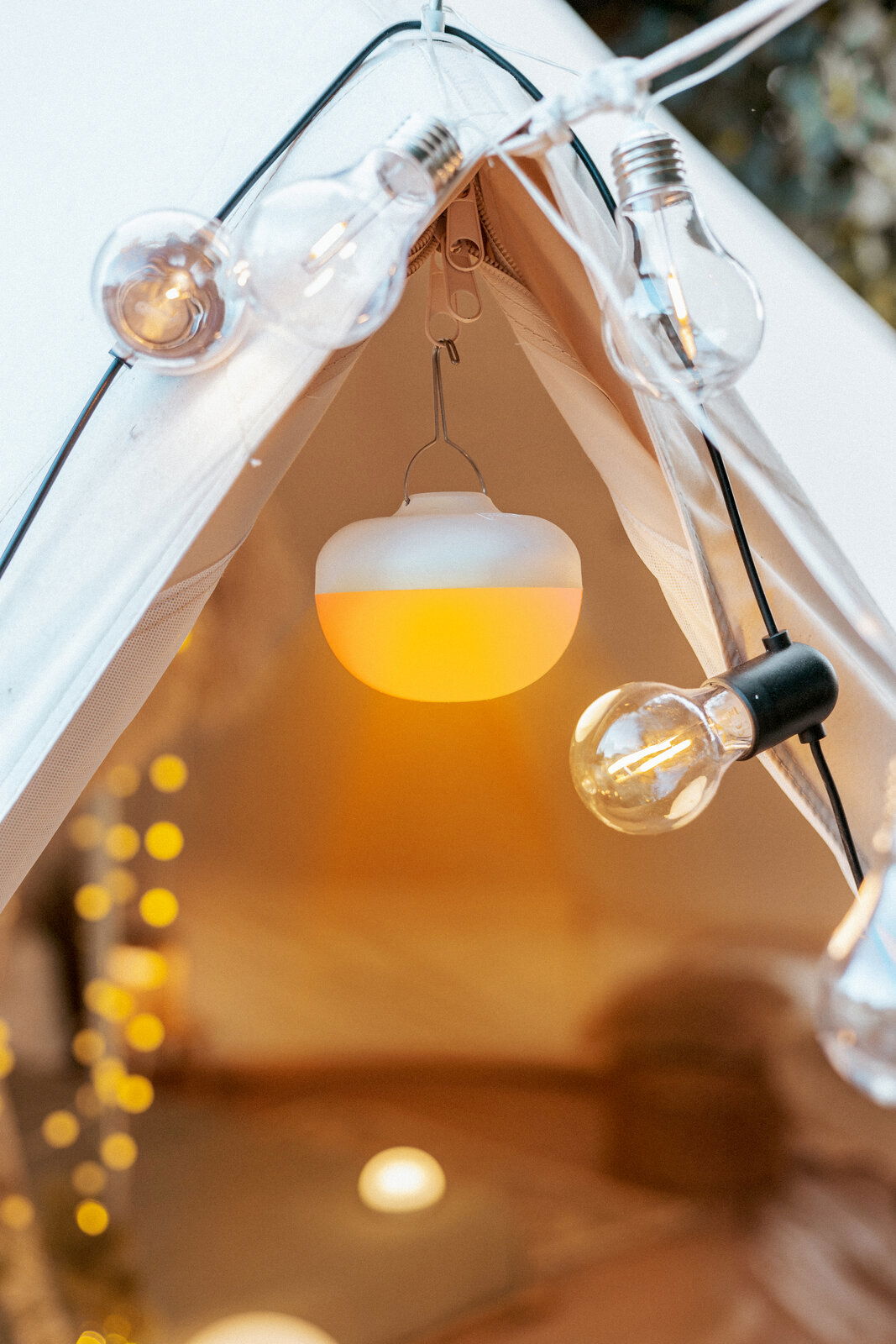 Akku-Leuchtmittel in einem Zelt, von innen betrachtet, umgeben von dekorativen Glühbirnen.