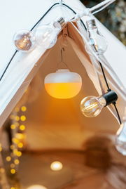 Akku-Leuchtmittel in einem Zelt, von innen betrachtet, umgeben von dekorativen Glühbirnen.