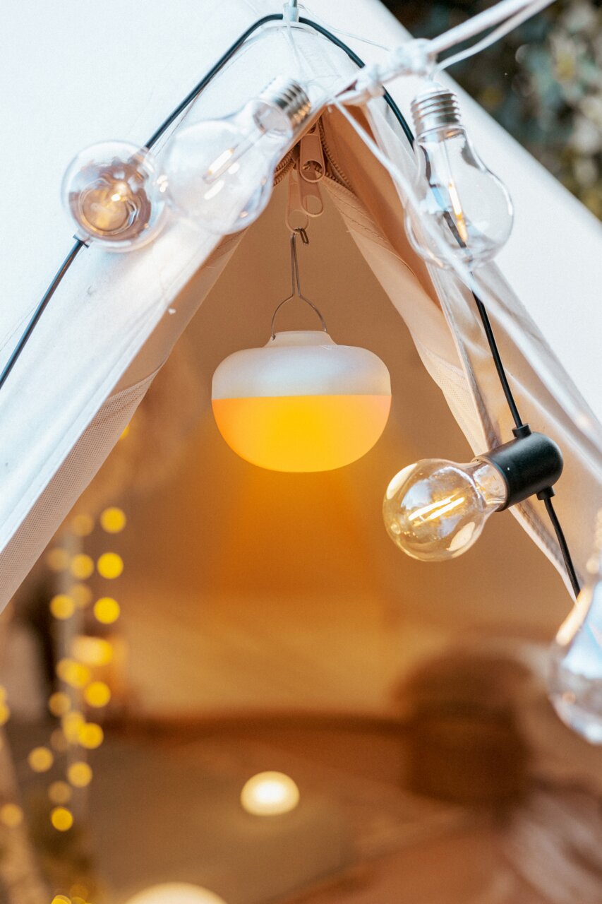 Newgarden Akku-Leuchtmittel CHERRY Akku-Leuchtmittel in einem Zelt, von innen betrachtet, umgeben von dekorativen Glühbirnen.