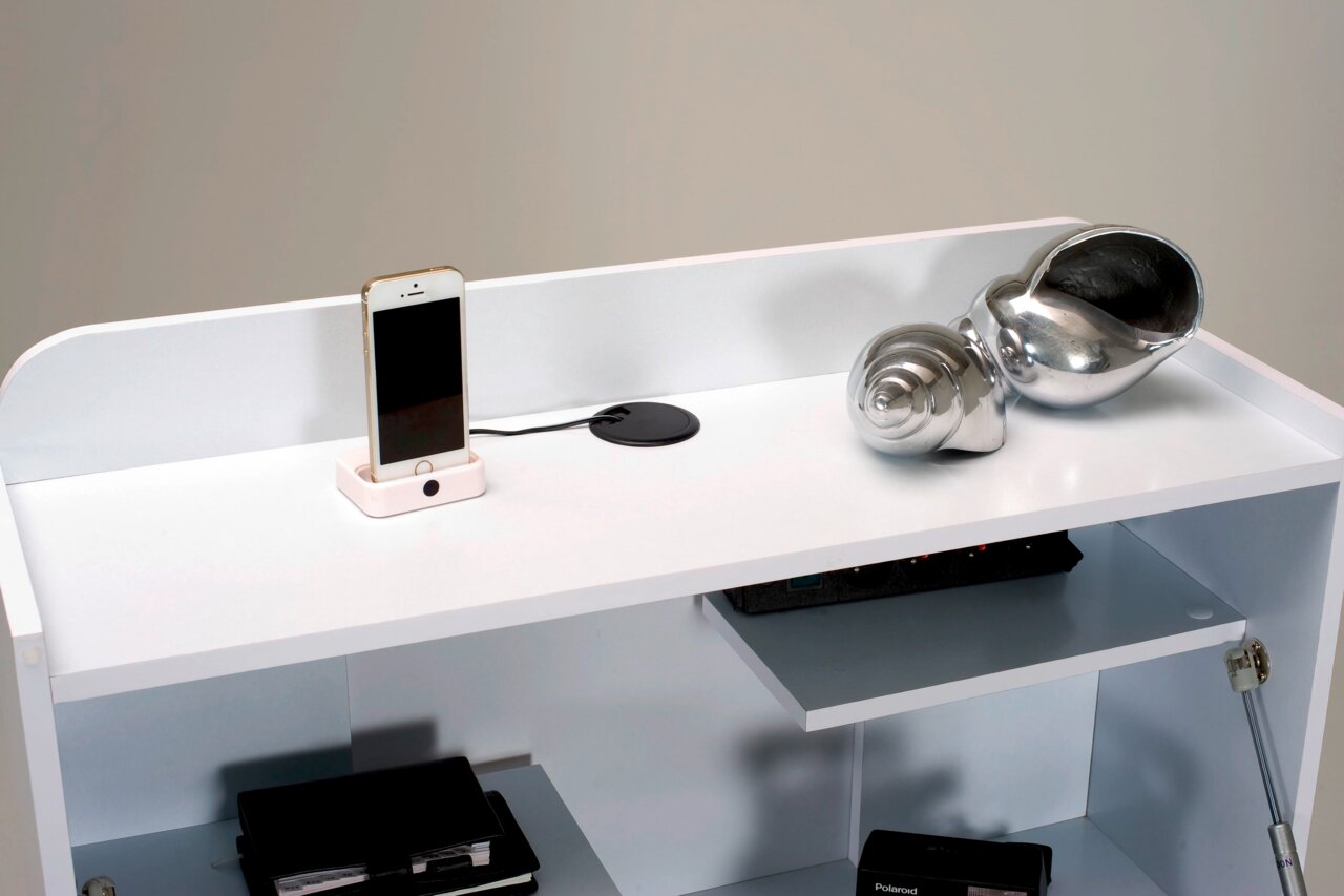 Witte secretaire met een legplank waarop een smartphone in een dockingstation en een zilveren decoratieve slak staan. Aanzicht van bovenaf.