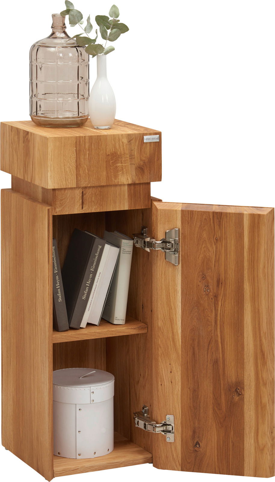 Beistelltisch aus Holz der Serie MAYA von Linea Natura, mit geöffneter Tür, Bücher und Dekoration darauf, aus seitlicher Perspektive.