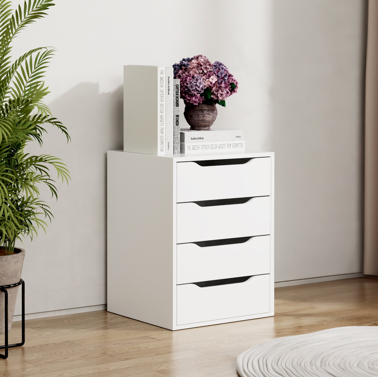 Weiße, moderne Kommode mit vier Schubladen und integrierten Griffmulden, dekoriert mit Büchern und einer Hortensie im Topf, im hellen Wohnraum aus leichter Frontansicht (leicht seitlich)