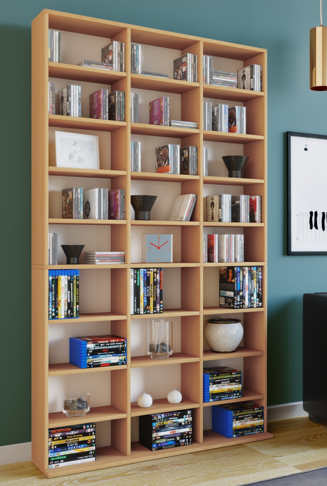 Großes, helles Holz-Bücherregal mit vielen Fächern, gefüllt mit Büchern und DVDs sowie Dekoration (Vasen, Kerzen, Uhr), in einem Wohnzimmer vor türkisfarbener Wand, fotografiert in frontaler Perspektive.
