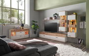 Wohnzimmer mit moderner Möbelkombination, bestehend aus Sideboard, TV-Lowboard und Hängeschränken in Holz- und Weißtönen, mit dekorativer Beleuchtung und Pflanzen, seitliche Perspektive.