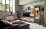 Wohnzimmer mit moderner Möbelkombination, bestehend aus Sideboard, TV-Lowboard und Hängeschränken in Holz- und Weißtönen, mit dekorativer Beleuchtung und Pflanzen, seitliche Perspektive.