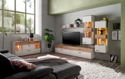 Wohnzimmer mit moderner Möbelkombination, bestehend aus Sideboard, TV-Lowboard und Hängeschränken in Holz- und Weißtönen, mit dekorativer Beleuchtung und Pflanzen, seitliche Perspektive.