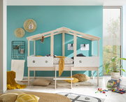 Spielbett in Hausform aus hellem Holz mit weißem Geländer, dekoriert mit Kissen und Decken, in einem Kinderzimmer mit türkisfarbener Wand. Perspektive: Frontalansicht.