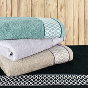 Ein Stapel von Handtüchern in verschiedenen Farben, darunter Türkis, Grau und Beige, mit dekorativen Mustern, auf einem dunklen Handtuch liegend. Perspektive von der Seite.