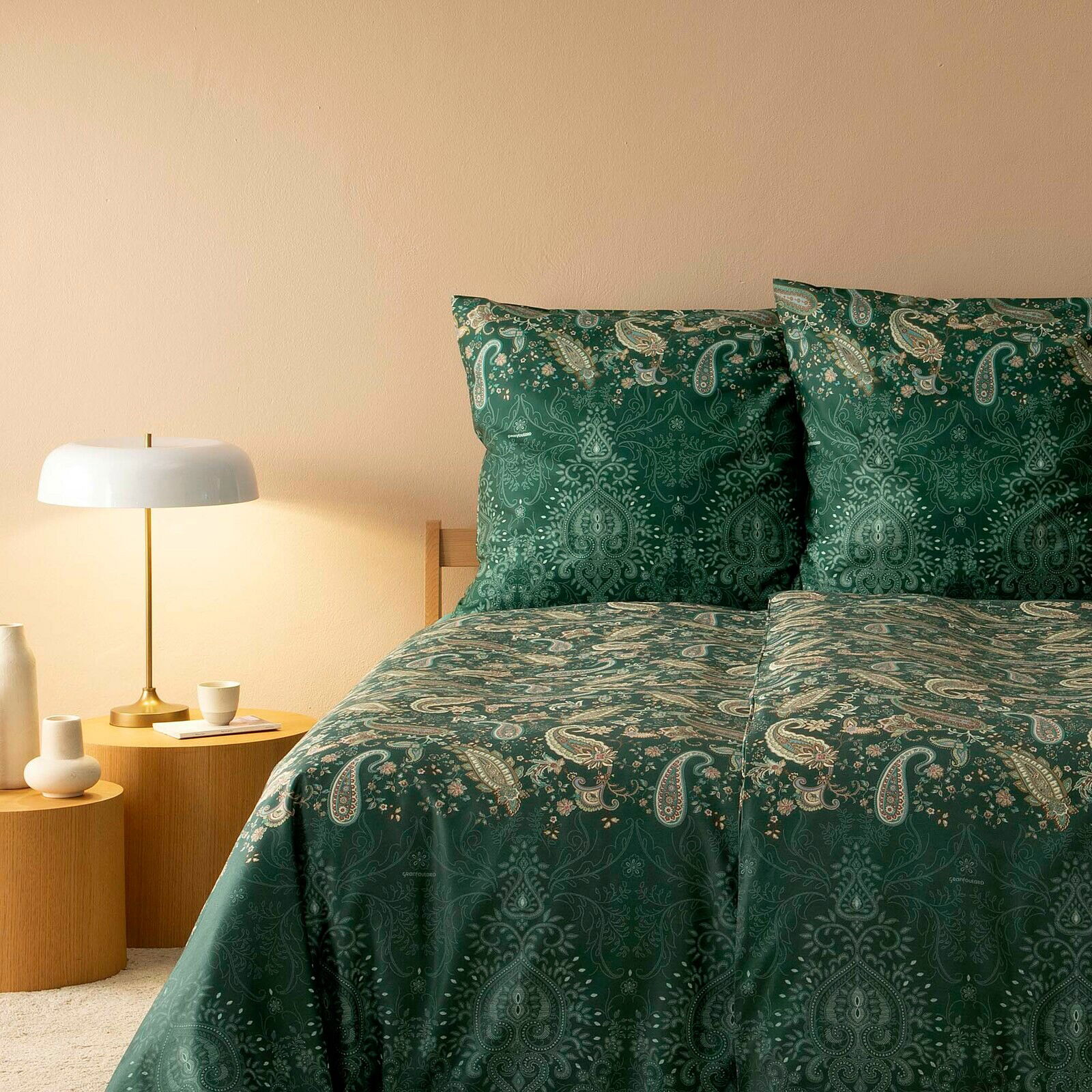 Grüne Bettwäsche mit Paisley-Muster auf einem Bett, seitliche Perspektive mit Nachttisch und Lampe.
