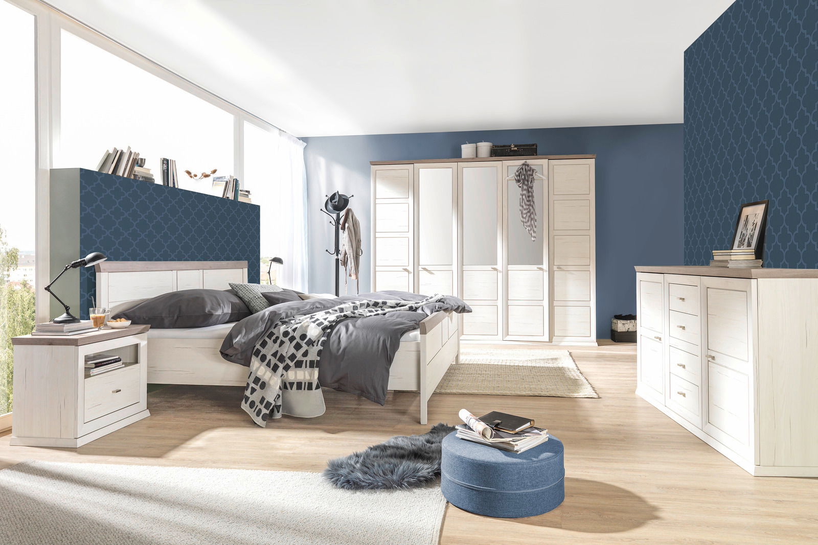 Helles Schlafzimmer mit einem großen Bett, einem fünftürigen Drehtürenschrank und einem Sideboard, seitliche Perspektive