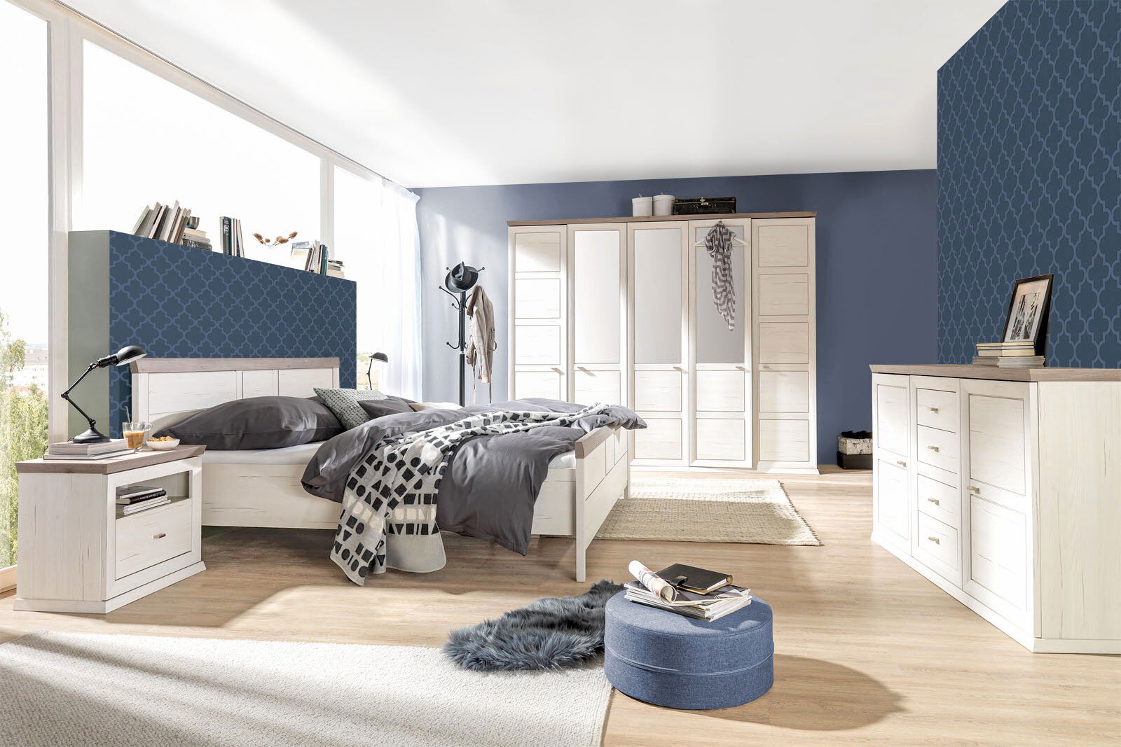 Helles Schlafzimmer mit einem großen Bett, einem fünftürigen Drehtürenschrank und einem Sideboard, seitliche Perspektive