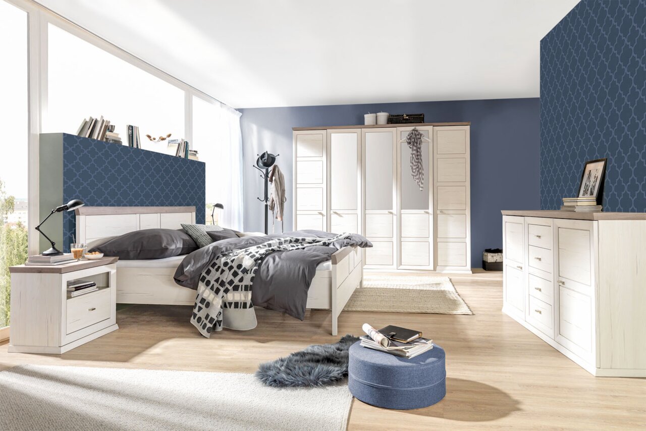 Helles Schlafzimmer mit einem großen Bett, einem fünftürigen Drehtürenschrank und einem Sideboard, seitliche Perspektive