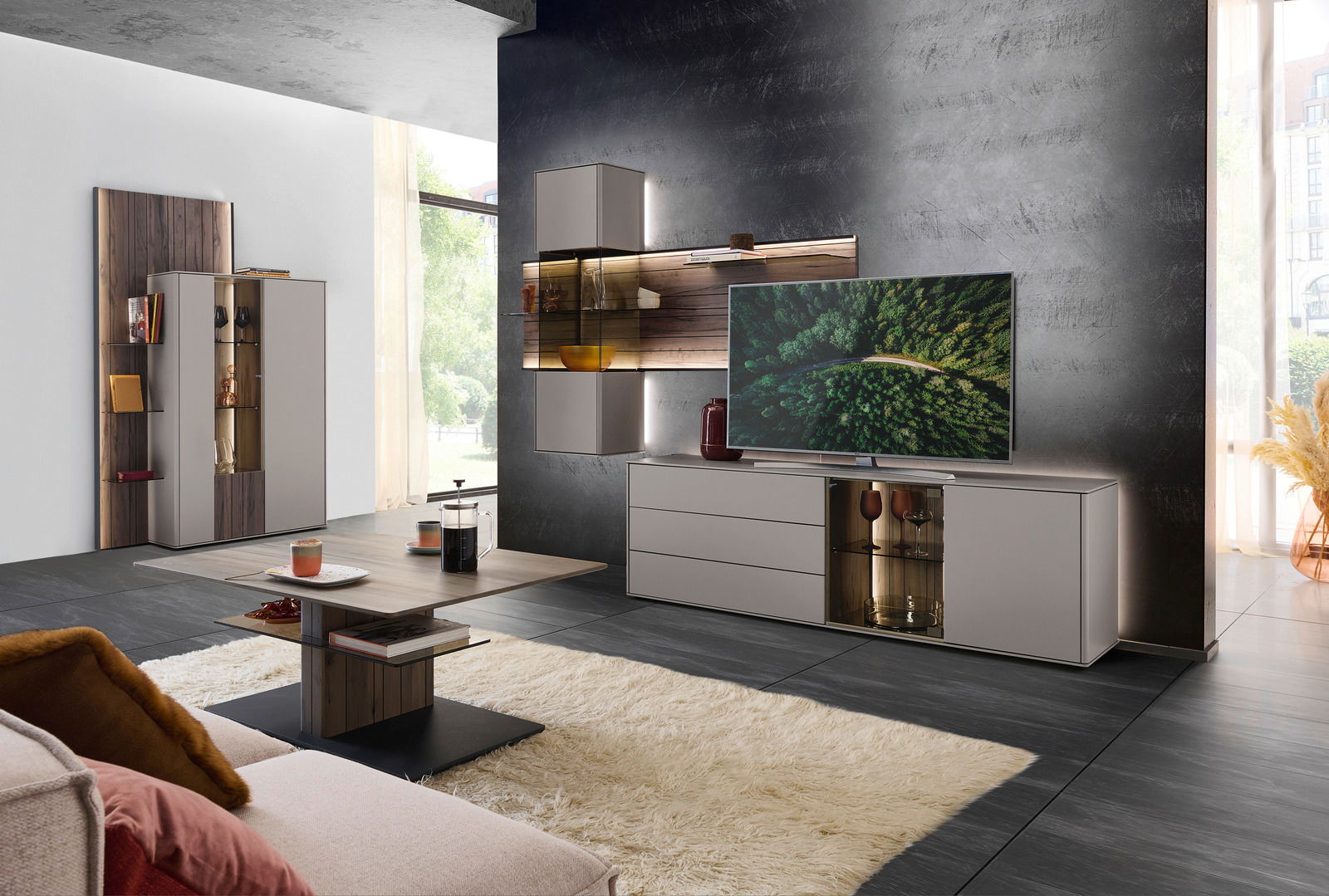 Moderne Wohnzimmer-Wandkombination in einer stilvollen Perspektive, bestehend aus einem TV-Schrank, Hängeschränken und Regalen in Holz- und Grautönen, mit dekorativen Elementen und einem großen Fernseher.