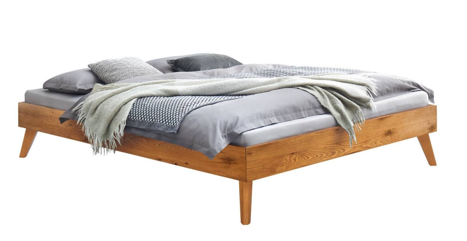 Modern houten bed met een laag frame en schuine poten, met grijs beddengoed, kussens en een deken, in een schuin zijaanzicht (3/4-perspectief) tegen een witte achtergrond.