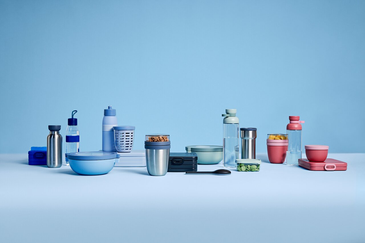 Een collectie drinkflessen en bekers in verschillende kleuren, waaronder een in Vivid Mauve, op een lichtblauwe achtergrond. De producten komen uit de VITA-serie van Mepal en worden vanuit een vooraanzicht getoond.