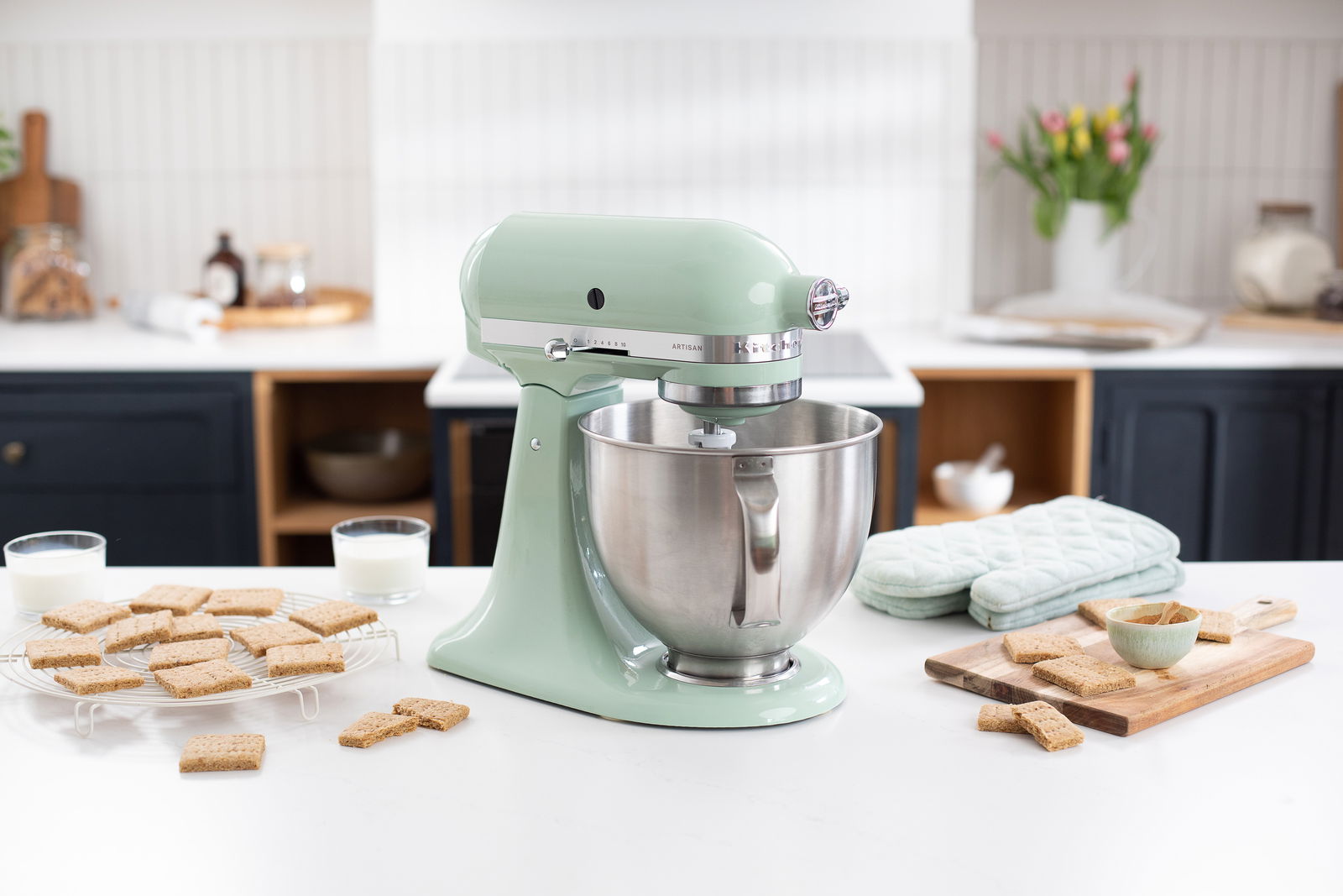 Küchenmaschine Artisan in Pastellgrün auf einer Küchenarbeitsplatte, seitliche Perspektive, umgeben von Keksen und Milchgläsern.