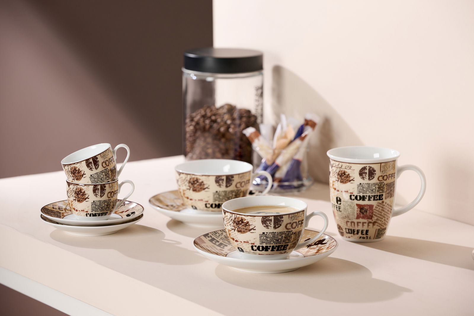 Vier Cappuccino-Tassen mit Untertassen, dekoriert mit Kaffeebohnen- und Schriftmotiven, auf einem Tisch arrangiert. Perspektive von schräg oben.