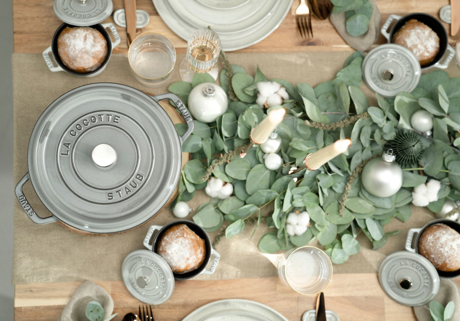 Vogelperspektive auf einen gedeckten Tisch mit einem grauen Bräter Cocotte 24cm rund von Staub, umgeben von grünem Eukalyptus und Kerzen.