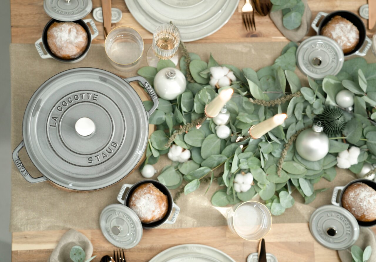 Vogelperspektive auf einen gedeckten Tisch mit einem grauen Bräter Cocotte 24cm rund von Staub, umgeben von grünem Eukalyptus und Kerzen.