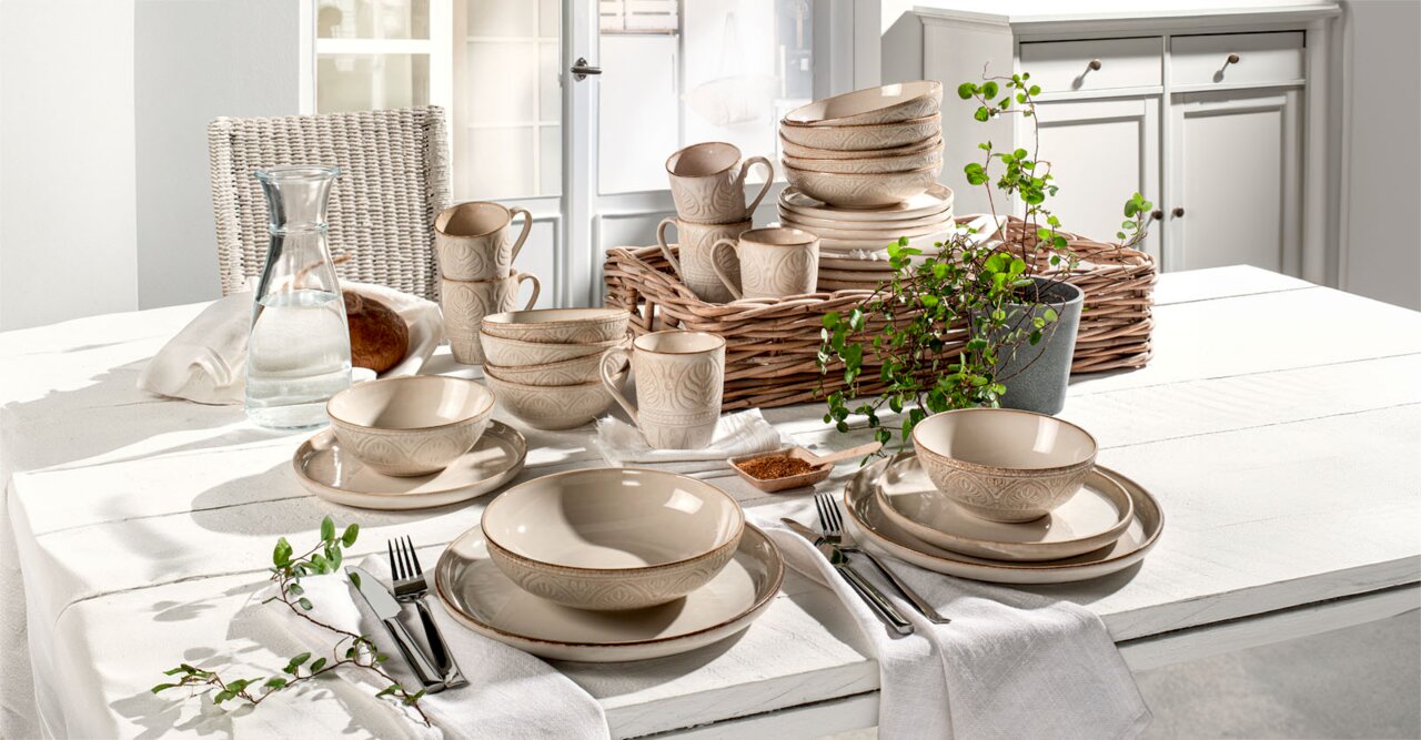 Kombiservice 30-teilig in beige mit elegantem Muster, arrangiert auf einem gedeckten Tisch in heller, einladender Umgebung. Perspektive von vorne.