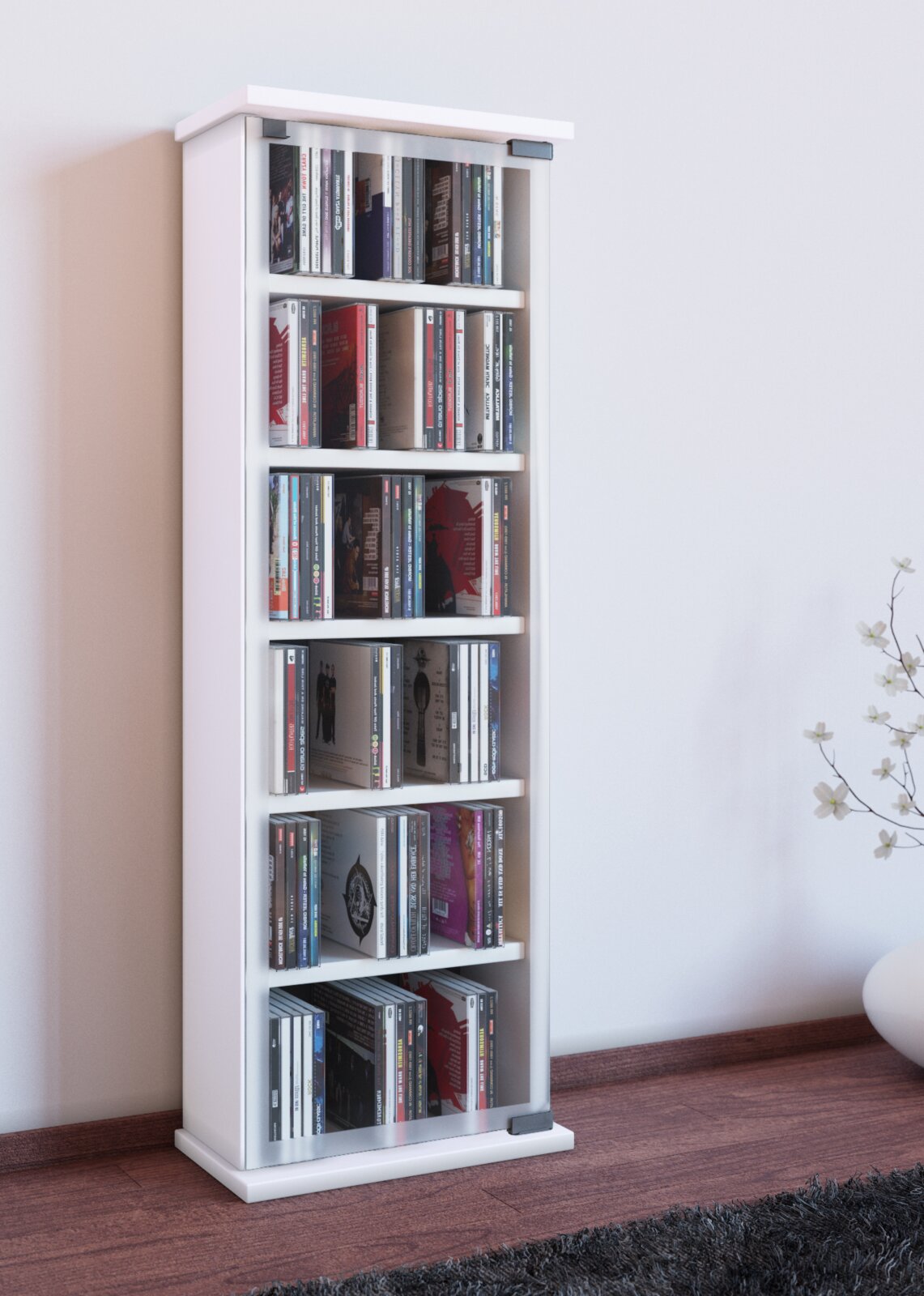 Weißes, schmales CD-/DVD-Regal mit Glastür und mehreren Fächern, gefüllt mit CDs, freistehend an einer Wand im Wohnzimmer, Frontansicht leicht schräg von links.