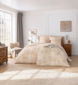 Elegante Bettwäsche in einem hellen, gemusterten Design auf einem Doppelbett in einem stilvoll eingerichteten Schlafzimmer mit Tageslicht von der linken Seite.