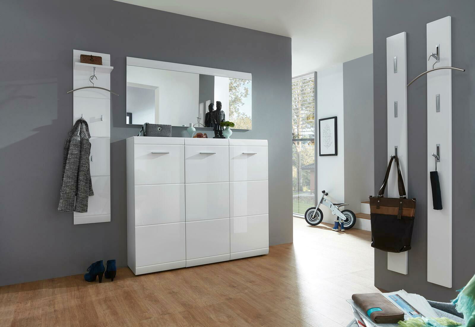 XORA Garderobenpaneel AVILA Moderner Eingangsbereich mit weißem Hochglanz-Schuhschrank, großem Spiegel und Garderobenpaneelen, seitliche Perspektive.