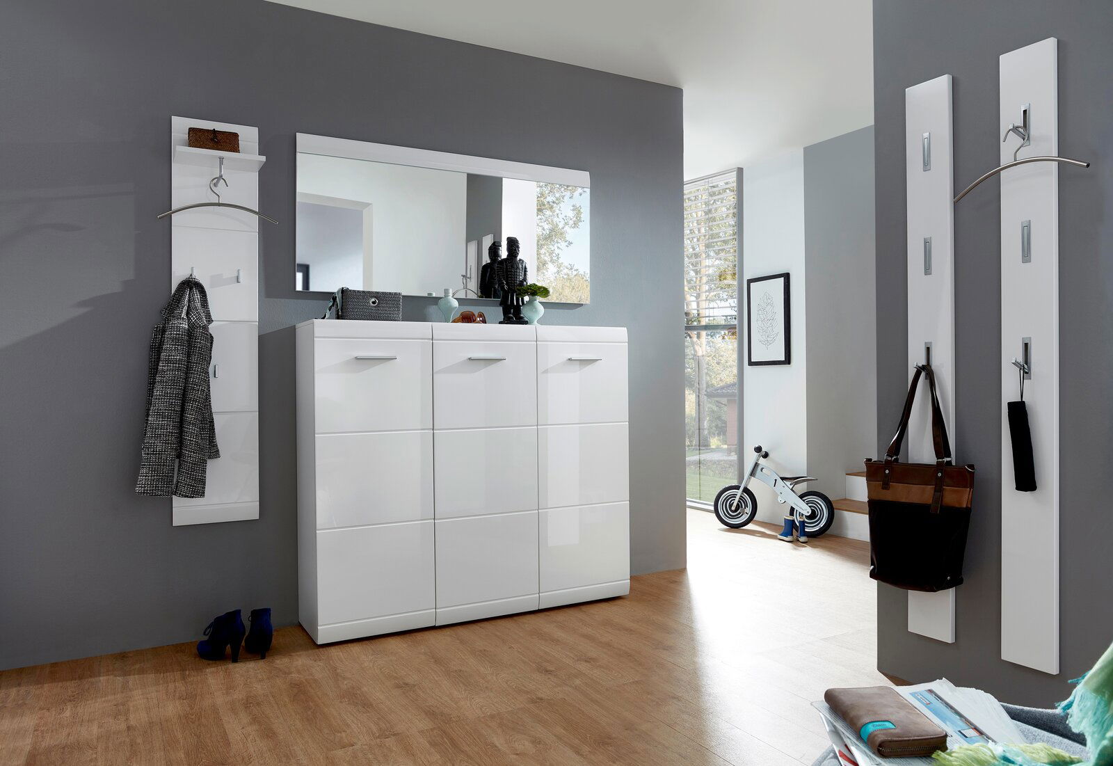 Moderner Eingangsbereich mit weißem Hochglanz-Schuhschrank, großem Spiegel und Garderobenpaneelen, seitliche Perspektive.