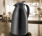 Schwarze, matte Isolierkanne mit 1 Liter Fassungsvermögen, frontal auf einem Tisch in einem Café platziert.