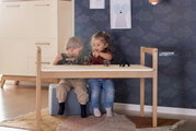 Twee kinderen spelen met dierenfiguurtjes op een tafelblad in een kinderkamer. Het tafelblad maakt deel uit van de Tiny Table, gemaakt van licht hout, met een modern en minimalistisch ontwerp. Perspectief: vooraanzicht van de tafel.