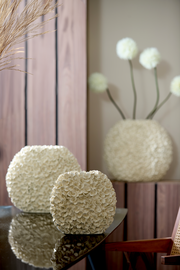 Nahaufnahme einer dekorativen Vase mit blütenförmiger Struktur auf einem Tisch, im Hintergrund weitere Vasen und Dekorationen.