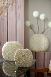 Nahaufnahme einer dekorativen Vase mit blütenförmiger Struktur auf einem Tisch, im Hintergrund weitere Vasen und Dekorationen.