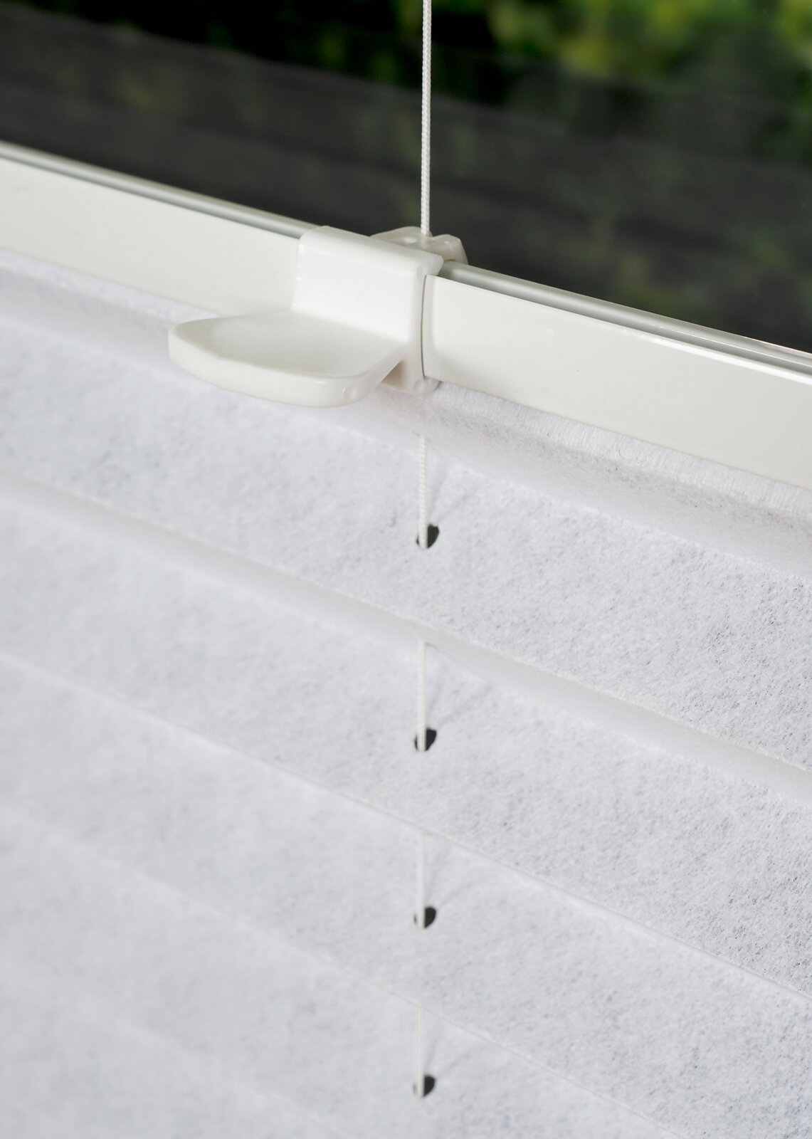 Nahaufnahme eines weißen, gefädelten Plissees an einem Fenster, seitliche Perspektive