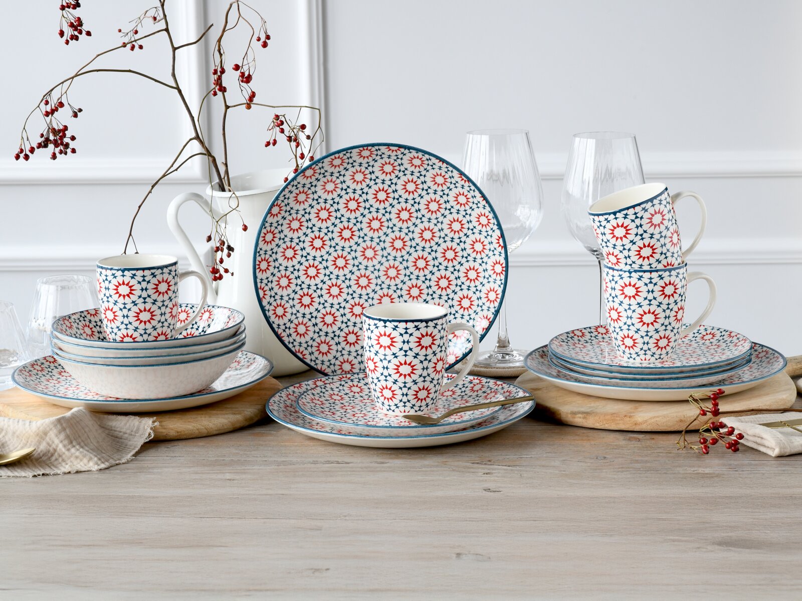 Creatable Kombiservice 16-tlg STELLA Frontale Tischansicht eines gemusterten Geschirrsets aus Porzellan mit Tellern, Schalen und Tassen in Weiß mit blau-rotem Sternmuster, dekorativ arrangiert neben Gläsern und einer weißen Kanne.