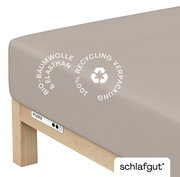 Spannbettlaken XL aus Bio-Baumwolle und Elasthan in Beige, Perspektive von der Ecke des Bettes, mit Hinweis auf 100% Recycling-Verpackung.