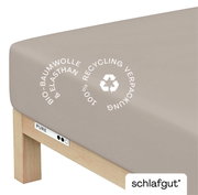 Spannbettlaken XL aus Bio-Baumwolle und Elasthan in Beige, Perspektive von der Ecke des Bettes, mit Hinweis auf 100% Recycling-Verpackung.