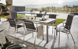 Moderner Gartentisch mit sechs Stapelsesseln auf einer Terrasse mit Blick auf einen Pool und eine Landschaft im Hintergrund, seitliche Perspektive.